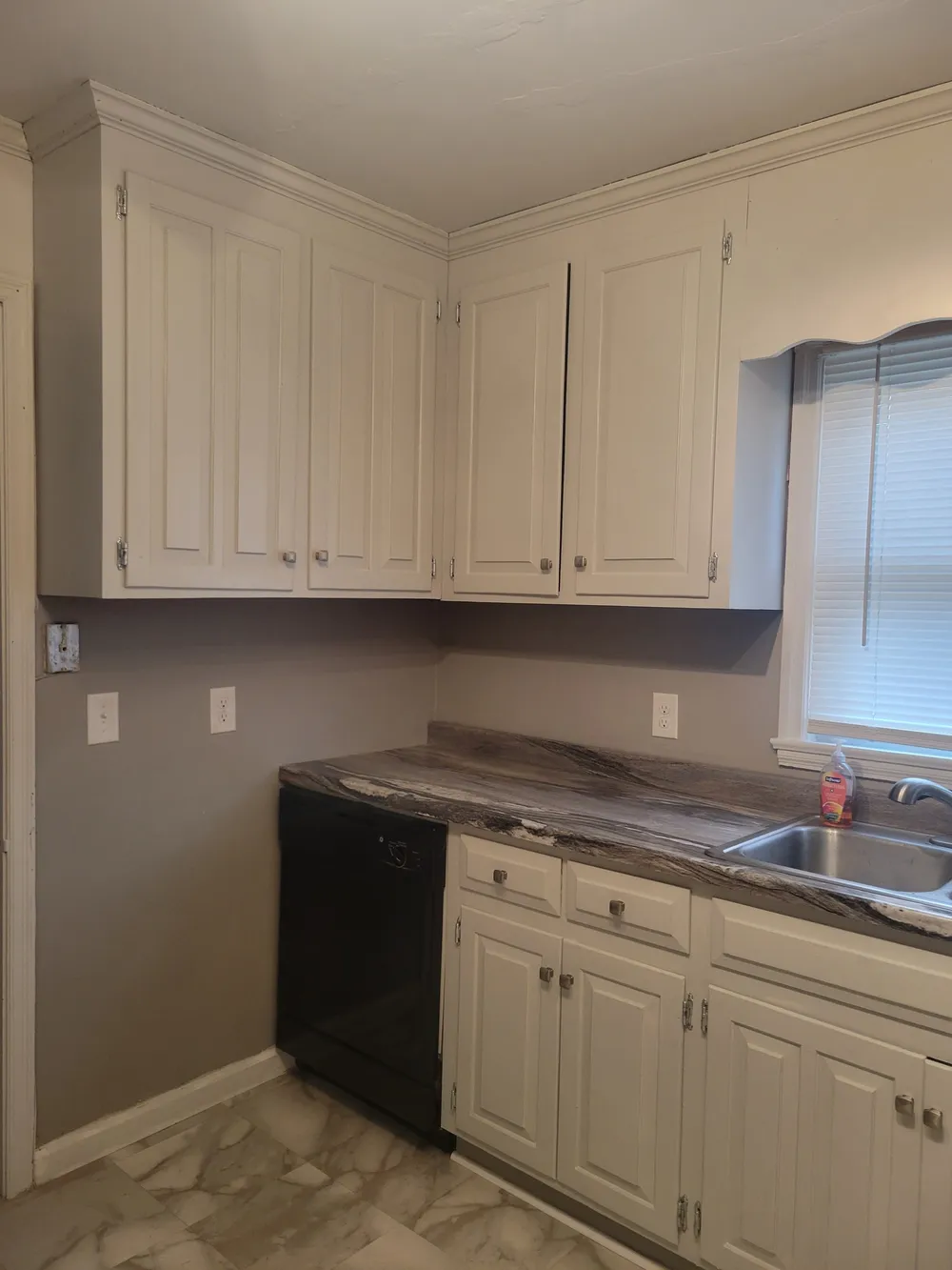 Kitchen corner with white cabinets, a black dishwasher and a window over the sink