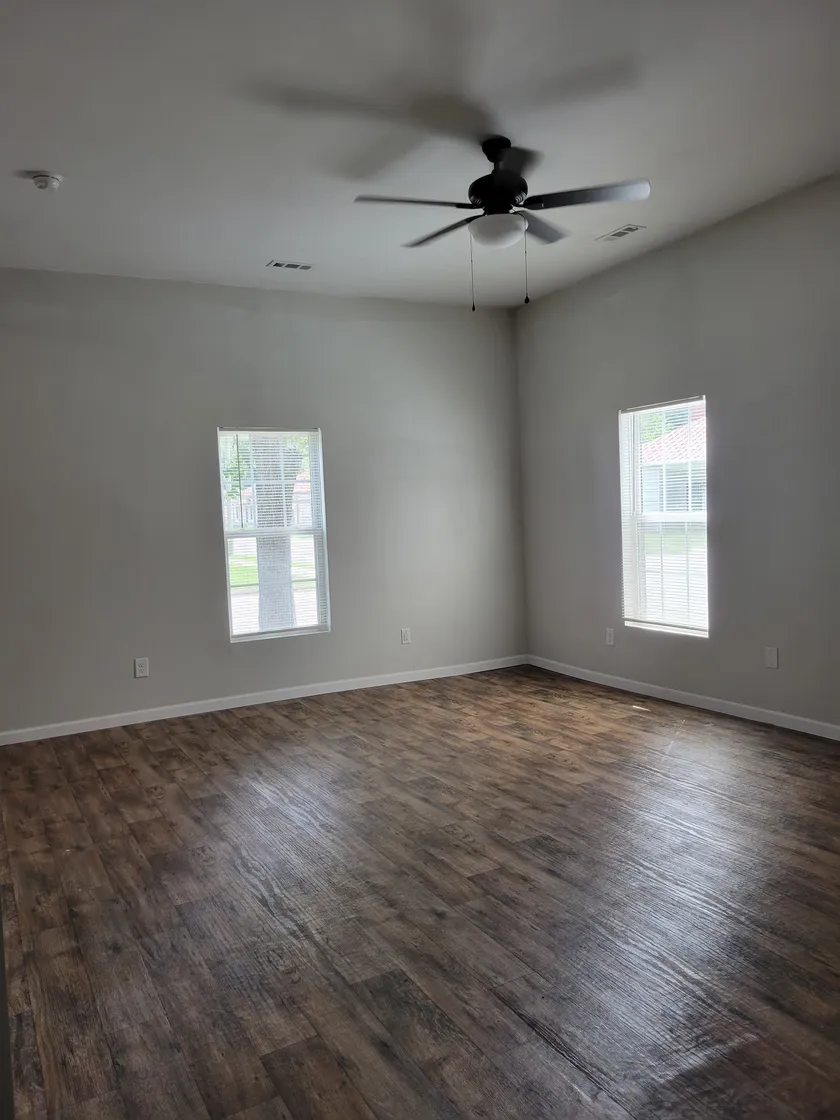 Empty room with wood-tone flooring, a ceiling fan and two windows